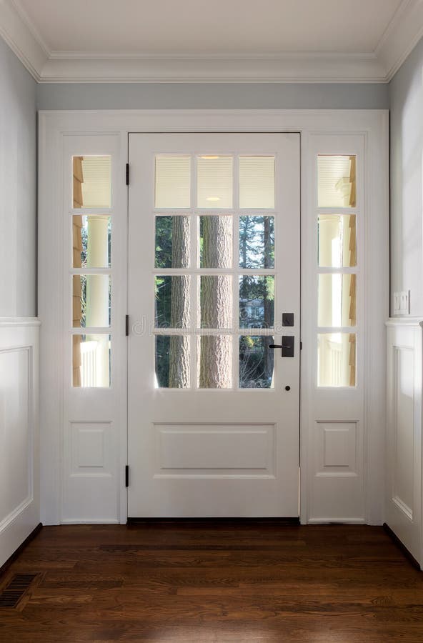 Vertical shot of a closed, wooden front door. From the interior of an upscale home with windows stock photo